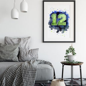 May include: Framed watercolor art print featuring the number 12 in green, with a cityscape silhouette, set against a blue and green watercolor background. The artwork is displayed in a black frame, suitable for home decor.