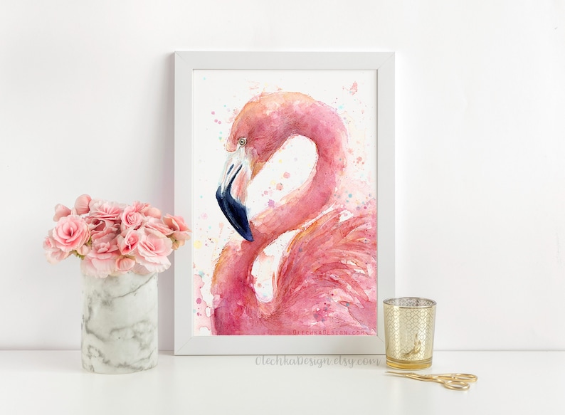 May include: A watercolor painting of a pink flamingo with a blue beak, set against a white background with colorful watercolor splatters. The painting is framed in a white frame.