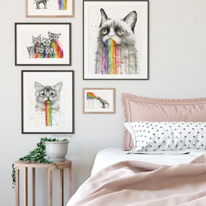 May include: A bedroom interior with a pink bedspread and a white pillow with black crosses. There are five framed black and white watercolor paintings on the wall, featuring a cat, an elephant, and kittens, all vomiting rainbows.