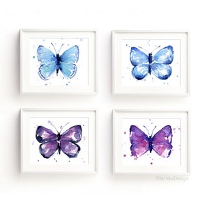 May include: Four watercolor paintings of butterflies in white frames. The butterflies are blue, purple, and pink. The paintings are arranged in a grid pattern on a white wall.