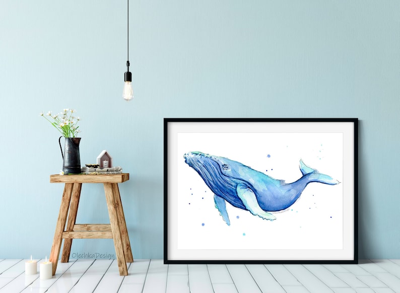May include: A watercolor painting of a blue whale swimming in the ocean. The whale is painted in shades of blue and white, with a white background. The painting is framed in a black frame.
