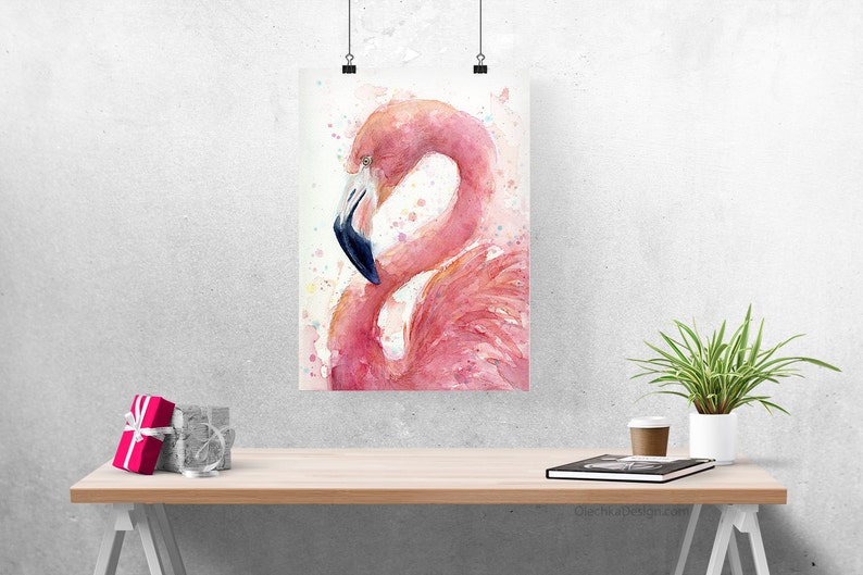 May include: A watercolor painting of a pink flamingo with a blue beak, standing on one leg with its head tucked into its feathers. The background is a light wash of pink and white with splatters of color.