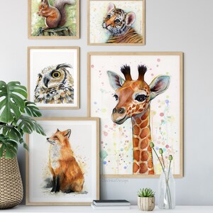 May include: A set of five framed watercolor paintings featuring various animals. The paintings include a squirrel, a tiger cub, an owl, a giraffe, and a fox. The paintings are all in a light wood frame and are arranged on a white wall.