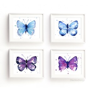 May include: Four watercolor paintings of butterflies in white frames. The butterflies are blue, purple, and pink. The paintings are arranged in a grid pattern on a white wall.