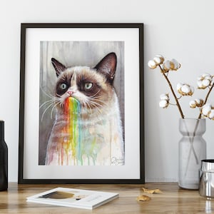 May include: A watercolor painting of a grumpy cat with a rainbow coming out of its mouth. The cat is looking at the viewer with a grumpy expression. The painting is framed in a black frame.