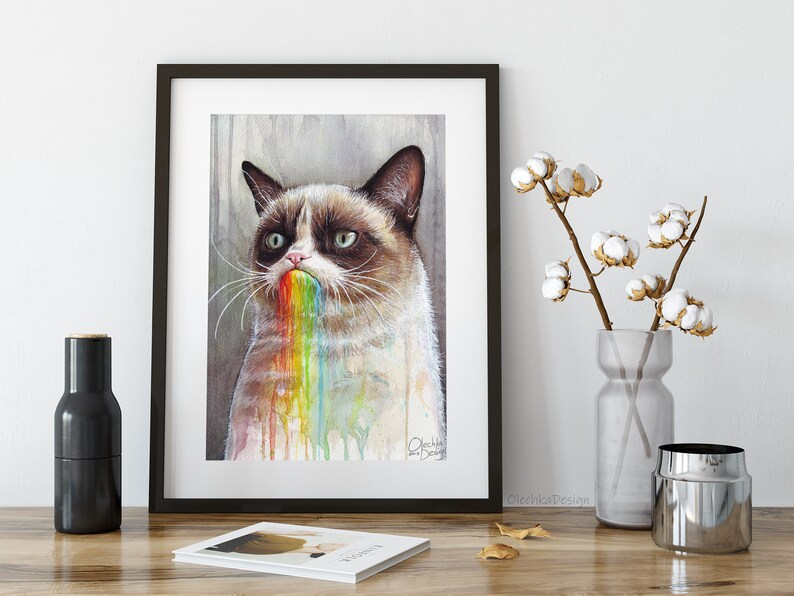 May include: A watercolor painting of a grumpy cat with a rainbow coming out of its mouth. The cat is looking at the viewer with a grumpy expression. The painting is framed in a black frame.