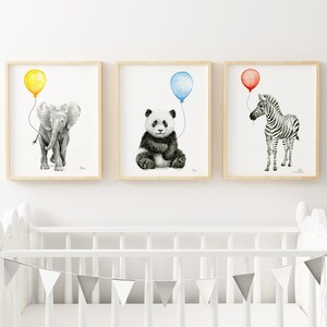 May include: Three framed watercolor prints featuring animals holding balloons. An elephant with a yellow balloon, a panda with a blue balloon, and a zebra with a red balloon. The prints are in light wood frames, perfect for a nursery.