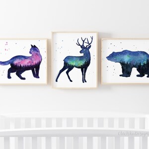 May include: Three watercolor prints featuring silhouettes of a cat, deer, and bear with a starry night sky and forest scene inside each animal.