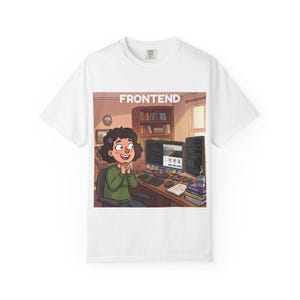 May include: A white t-shirt featuring a graphic illustration of a person sitting at a desk with a computer, books, and a mug. The text FRONTEND is printed in white at the top of the graphic, which depicts a workspace with a bookshelf and monitors.