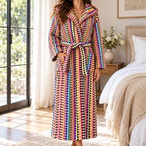 May include: A floor-length bathrobe featuring a vibrant, multi-colored crochet-style pattern with repeating geometric shapes in shades of red, yellow, blue, pink, and black. The robe includes a hood, long sleeves, two front pockets, and a matching tie belt.