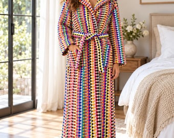 Op de afbeelding: Een kamerjas tot op de grond met een levendig, meerkleurig haakpatroon met herhalende geometrische vormen in tinten rood, geel, blauw, roze en zwart. De jas is voorzien van een capuchon, lange mouwen, twee voorzakken en een bijpassende ceintuur.