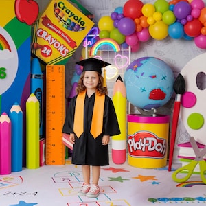 Könnte beinhalten: Ein Kind in einem Abschlusskleid und einer Kappe steht vor bunten Schulmaterialien. Die Szene umfasst einen Regenbogen, Buntstifte, Bleistifte, einen Globus und einen Play-Doh-Behälter. Ein Lineal zeigt cm-Maße. Im Hintergrund befindet sich ein Luftballonbogen.