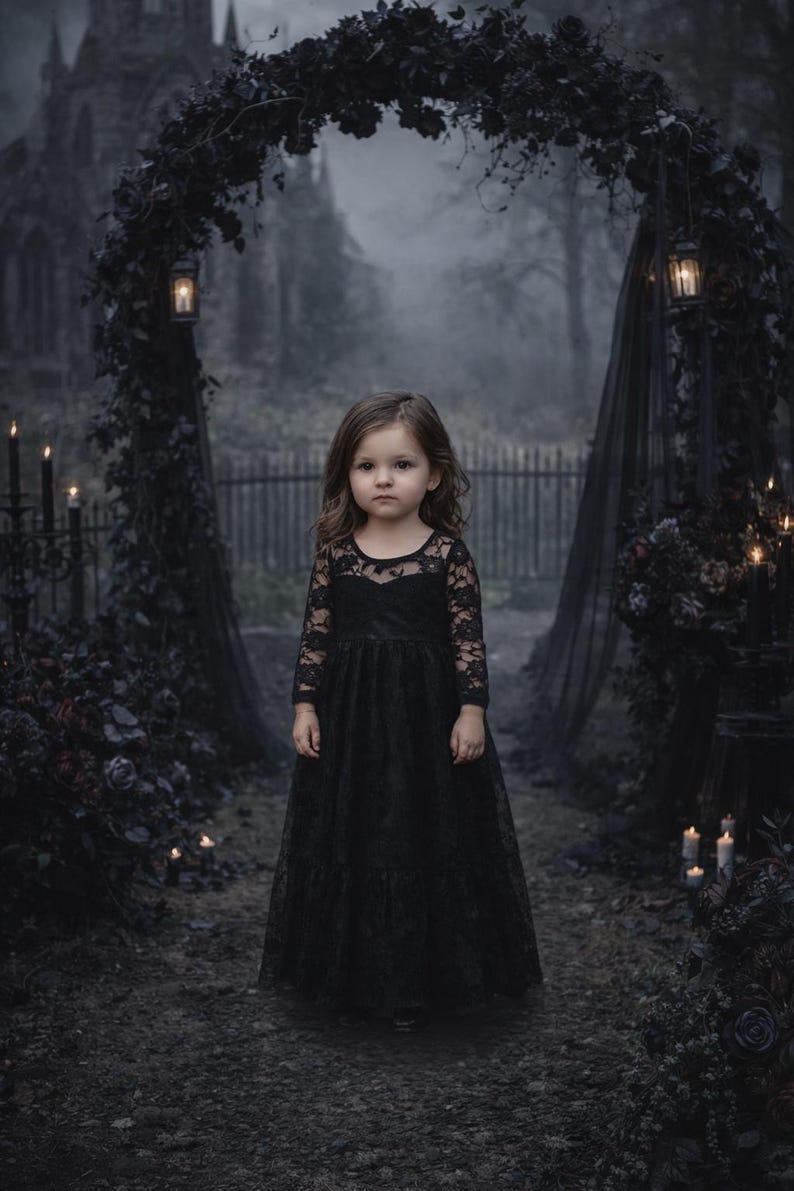 Puede incluir: Una ni&ntilde;a con un vestido negro de encaje se encuentra en un entorno g&oacute;tico al aire libre. El vestido tiene mangas largas y una falda de tul. El fondo incluye un arco oscuro, velas y una iglesia borrosa.