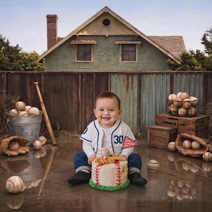 May include: A smiling baby wearing a baseball jersey with the number 30 sits in front of a cake decorated like a baseball. A baseball bat, glove, and bucket of baseballs are nearby. A small flag on the cake reads "Happy Birthday".