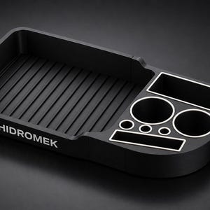 May include: A matte black organiser tray featuring the white text HIDROMEK. The tray includes a large rectangular ribbed section, two circular cup holders, two smaller circular openings, and two rectangular compartments with white trim and a clamp.
