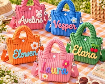 May include: Five corduroy tote bags in pink, blue, orange, and green, each featuring a white snap closure, a detachable shoulder strap, and a name embroidered in raised letters: Aveline, Vesper, Elowen, Laura, and Elara, with small floral or bunny accents.