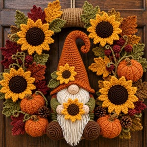 Könnte beinhalten: Ein Häkelkranz mit einem zentralen Wichtel mit hohem orangefarbenem Hut, weißem Bart und Sonnenblume. Der Kranz ist mit gelben Sonnenblumen, orangefarbenen Kürbissen, braunen Tannenzapfen und herbstlich gefärbten Blättern in Rot, Orange und Grün verziert.