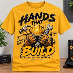 Puede incluir: Una camiseta color amarillo mostaza con un gráfico de un casco de seguridad amarillo y manos enguantadas sosteniendo un martillo y una llave inglesa. El texto dice: HANDS THAT BUILD, BUILD FIX IMPROVE REPEAT y HARD WORK BUILDS A BETTER TOMORROW, con una grúa.