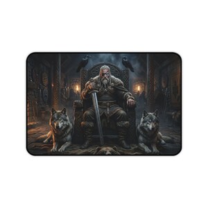May include: A rectangular desk mat featuring a bearded figure with an eyepatch sitting on a throne, holding a sword. Two grey wolves sit on either side of the throne, with two black ravens perched on the back of the chair in a dimly lit hall.