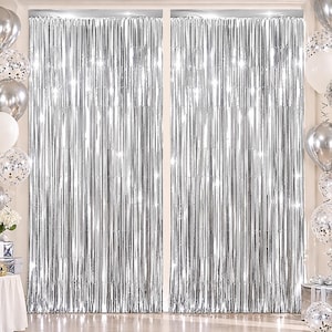 May include: Two shimmering silver metallic foil fringe curtains hanging side by side. The curtains feature long, thin vertical strips that reflect light, creating a bright, reflective surface. The fringe is suspended from a straight top edge.