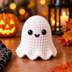 May include: A small, white, crocheted ghost figurine featuring a rounded top, a wavy bottom edge, and two black plastic safety eyes with a small black stitched mouth centered between them, creating a simple, rounded, and soft-textured appearance.