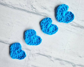 Puede incluir: Cuatro corazones de crochet azul dispuestos en fila sobre una superficie blanca texturizada.