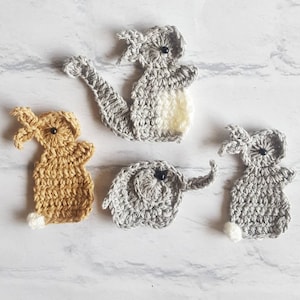 May include: Four crocheted animal appliques: a grey koala, a grey elephant, a grey bunny, and a tan bunny. The animals have black eyes and are made with a soft yarn.