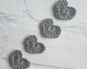 Puede incluir: Cuatro corazones de ganchillo grises dispuestos en fila sobre un fondo blanco.