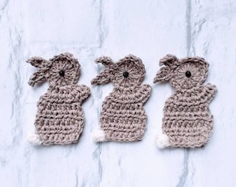May include: Three crocheted brown bunny rabbit ornaments with white tails. The bunnies have black button eyes.