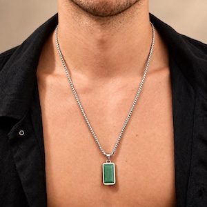 May include: A silver-toned box chain necklace featuring a rectangular pendant with a smooth, solid green stone inlay. The pendant is framed in a polished silver-colored metal setting and hangs from a classic link chain resting against the chest.