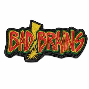 May include: An embroidered patch featuring the text BAD BRAINS in red letters with a green outline. A yellow lightning bolt graphic is positioned behind the letters. The entire design is bordered by a thick black stitched edge.