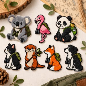 May include: A set of seven embroidered patches featuring a gray koala, a pink flamingo, a black and white panda, a black and white cat, an orange otter holding a branch, an orange fox, and a black and white dog, all wearing green backpacks.