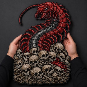 May include: A large embroidered patch featuring a detailed red and black centipede crawling over a pile of beige human skulls and bones. The design has a black border and intricate stitching that highlights the creature's many legs and segments.
