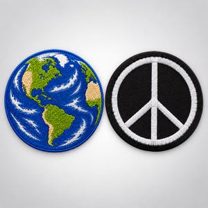 May include: Two circular embroidered patches. The left patch features a detailed depiction of the Earth with green continents, tan desert areas, and blue oceans with white swirling clouds. The right patch is black with a white peace symbol.
