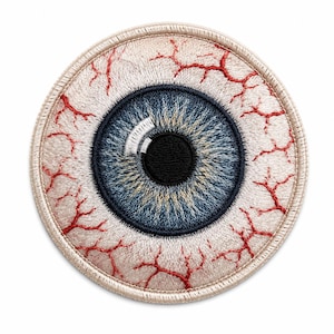 Op de afbeelding: Een ronde geborduurde patch met een realistisch menselijk oog. De iris is donkerblauw met een zwarte pupil en een witte reflectie. Het oogwit is gebroken wit met gedetailleerde rode stiksels die bloeddoorlopen adertjes voorstellen.