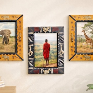May include: Three rectangular picture frames with decorative metal animal accents. Two outer frames are yellow with elephant motifs, while the central frame is black with red patterns and giraffe accents, displaying photographs of wildlife and a person.