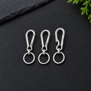 May include: Three silver-colored metal carabiner keychains with attached circular split rings. Two carabiners feature a standard spring-loaded gate, while the third carabiner includes an integrated bottle opener notch on the side of the frame.