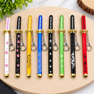 May include: Eight katana-style pens with gold-colored guards and attached keychains. The pens feature various designs including pink cherry blossoms on white, black with pink flowers, yellow with a dragon, blue waves, black with stars, green with bamboo, black with a white dragon, and red with flames.