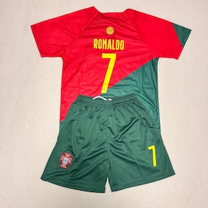 Peut inclure: Un maillot de football rouge et vert avec le nom RONALDO et le numéro 7 en jaune au dos, accompagné d'un short vert assorti affichant le numéro 7 en jaune et un petit écusson sur la jambe gauche du short.