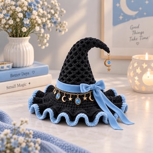 May include: A black crocheted witch hat with a light blue velvet ribbon and bow. The hat features a gold-toned chain with alternating star and crescent moon charms, plus blue oval cabochons. The brim edge is trimmed in light blue yarn.