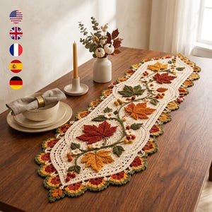 Pode incluir: Um caminho de mesa de crochê na cor creme com um padrão intrincado de folhas de bordo de outono tridimensionais em tons de vermelho, laranja e verde, acentuado com pequenas flores brancas e cachos de bagas ao longo de uma borda de vinha.