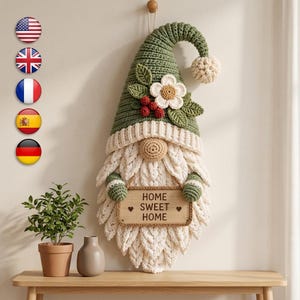 May include: A crocheted wall hanging shaped like a gnome with a tall green hat, a cream-colored beard, and a flower accent. The gnome holds a rectangular wooden sign with the text HOME SWEET HOME and two small heart symbols engraved on it.