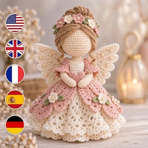 Puede incluir: Una muñeca ángel de ganchillo con cabello de hilo marrón claro recogido en un moño, adornado con una corona de flores. La muñeca viste un vestido color crema con una falda rosa de capas festoneadas, flores blancas y alas con perlas.
