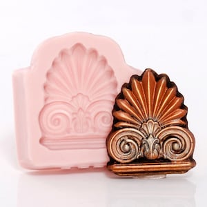 May include: A pink silicone mold for making decorative cake toppers. The mold features a detailed design of a shell with scrolls and a base. A finished cake topper made with the mold is shown in bronze.