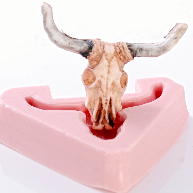 May include: A pink silicone mold shaped like a bull's head with a detailed bull skull sculpture inside.