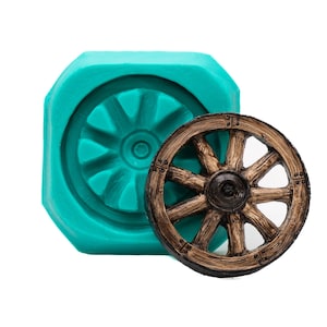 May include: A teal silicone mould with a circular recessed pattern and a finished brown wooden wagon wheel replica with eight spokes and a central hub, showing detailed wood grain texture and small metal-like rivets on the rim.