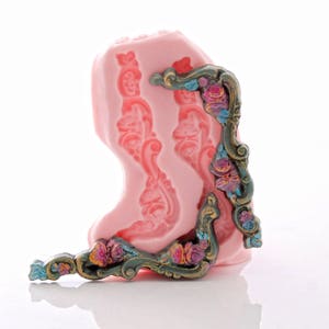 May include: A pink silicone mold with two detailed floral designs. The mold is used to create decorative cake borders or other edible embellishments.