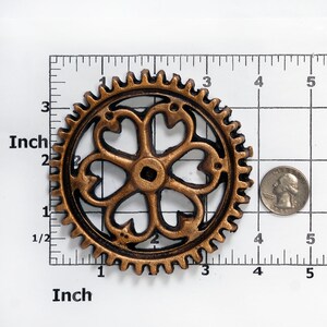 May include: A gold-colored metal gear with a decorative, black, five-pointed star design in the center. The gear is approximately 2 inches in diameter.