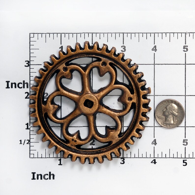 May include: A gold-colored metal gear with a decorative, black, five-pointed star design in the center. The gear is approximately 2 inches in diameter.