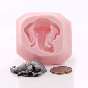 Puede incluir: Molde de silicona rosa para hacer una peque&ntilde;a figura de elefante. El molde tiene forma de diamante y presenta un dise&ntilde;o de elefante detallado. Se muestra una peque&ntilde;a figura de elefante gris junto al molde.